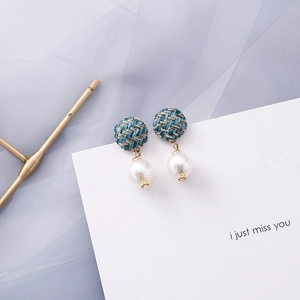 Detailed view of woven blue and gold studs with white pearls on elegant display