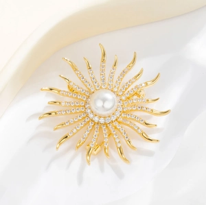 Broche de girasol dorado con perla central y circonitas brillantes sobre fondo de seda