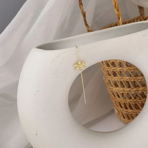 Detailed shot of golden snowflake earrings with pink zircons on a white ceramic vase