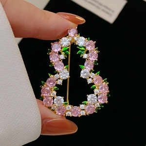 Dettaglio macro di spilla a fiore dorata con zirconi rosa e accenti di foglie verdi