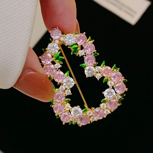 Dettaglio macro di una spilla a zucca in zircone rosa con accenti di foglie verdi su oro