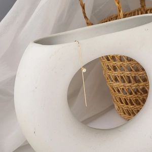 Detail of a minimalist gold hook earring with a zircon on a textured ceramic vase