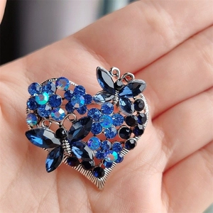 Detail of blue rhinestone heart brooch with butterfly and floral design held in hand