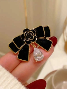 Macro de la broche nœud camélia en émail noir avec bordure dorée et zircon goutte