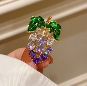 Détail d'une broche raisin de luxe avec strass violets et feuilles d'émail vert