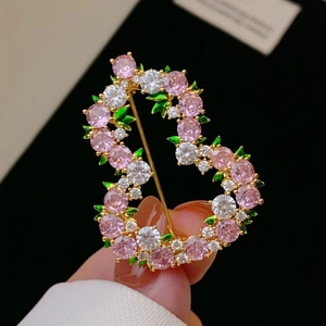 Macro di un'elegante spilla dorata a S con zirconi rosa e dettagli di foglie verdi