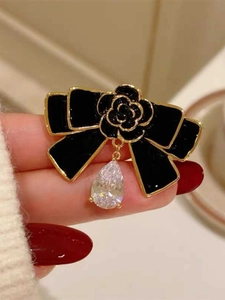 Détail d'une broche nœud vintage en émail noir avec camélia doré et pendentif en zircon
