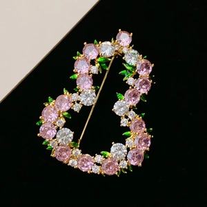 Dettaglio macro di una spilla floreale a forma di B con zirconi rosa e gemme verdi