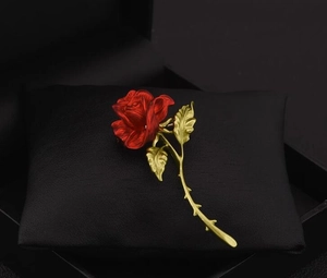 Detail of red rose brooch with golden stem on black jewelry cushion display