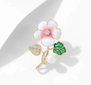 Détail de broche fleur aux pétales roses, feuilles dorées, cristal et perle blanche