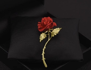 Detail of red rose brooch with golden stem resting on premium black jewelry cushion
