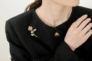 Close-up of golden rose brooch with pearl detail on black tweed fabric jacket