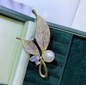 Vue macro d'une broche en forme de feuille dorée avec cristaux brillants et perle blanche