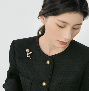 Detailed close-up of a golden rose brooch with a white pearl on a black tweed blazer lapel