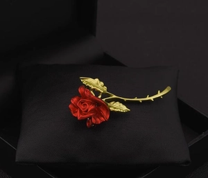Detail shot of a red rose brooch with golden stem on a black leather cushion