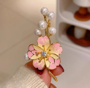 Détail macro d'une broche cerisier en émail rose avec base dorée et perles blanches