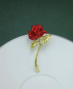 Detail showing vivid red rose brooch petals with golden leaf texture on green backdrop