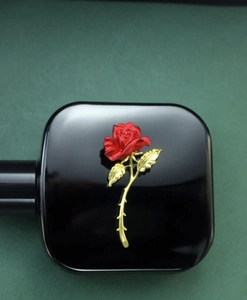 Close-up of red rose brooch with golden stem on black perfume bottle background