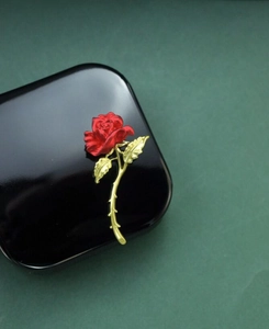 Macro detail of red enamel rose brooch with golden textured stem and leaf veins