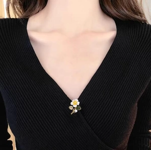 Élégante broche fleur en émail blanc avec centre jaune et feuille verte sur pull noir