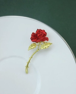 Close-up of a red enamel rose brooch with gold stem on a white ceramic plate
