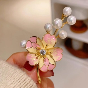 Gros plan d'une broche fleur de pêcher avec émail rose, perles et zircone dans la main