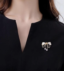 Elegant gold bow brooch with white shell inlay and hanging pearl tassels on black clothing