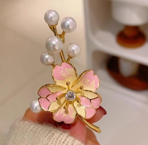 Détail d'une broche fleur de pêcher en émail rose avec perles et zircon à la main