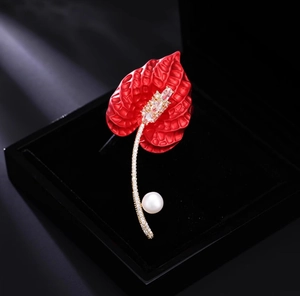 Detail of red calla lily brooch with shimmering crystals and a white pearl on black velvet
