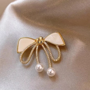 Elegant bow brooch with gold finish, sparkling zircons, and white hanging pearls on silk