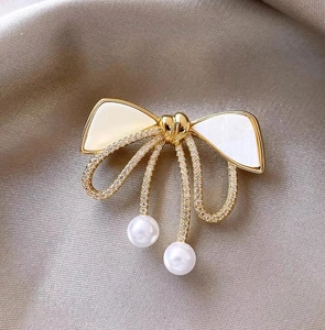Detail of elegant bow brooch with shimmering rhinestones and white pearls on silk background