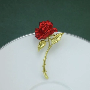 Elegant red rose brooch pin with golden stem on white porcelain dish decor