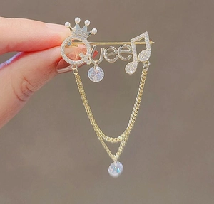 Detailed view of Queen letter brooch with gold tassels, crown, pearls and rhinestones