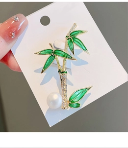 Detail of bamboo brooch featuring green enamel leaves and small inlaid crystals