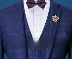 Detailed close-up of a golden crown lapel pin with rhinestones on a navy plaid suit