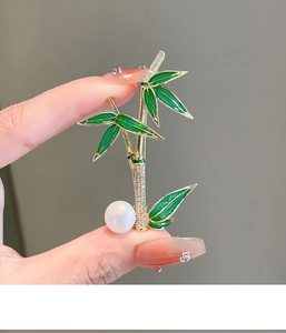 Macro detail of gold bamboo brooch with green enamel leaves, crystals, and white pearl