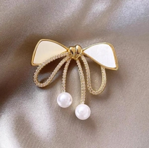 Macro detail of golden bow brooch with sparkling crystals and elegant white pearls