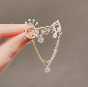 Detail view of Queen letter brooch with rhinestones, pearls and golden tassels