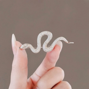 Primo piano di una mano che regge l'elegante spilla a serpente con zirconi bianchi intarsiati