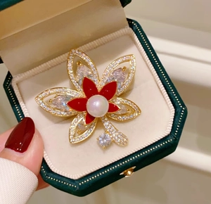 Dettaglio della spilla a fiore dorata con petali rossi, perla centrale e zirconi lucidi