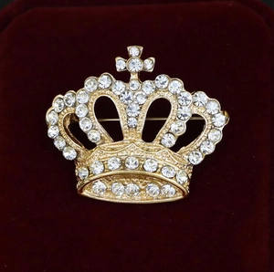 Detailed view of a gold crown brooch with sparkling rhinestones on red velvet fabric