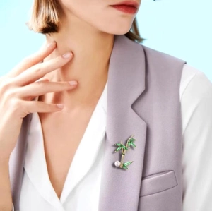 Elegant bamboo brooch with green enamel leaves and pearl accent on a gray vest