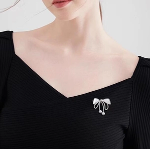 Close-up of a silver bow brooch with white pearls and tassel on a black v-neck sweater