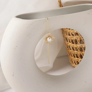 Detail of gold flower drop earring with pave crystals and pearl on a white vase