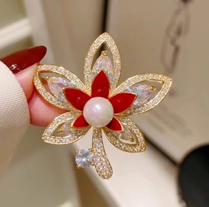 Dettaglio di elegante spilla a foglia d'acero con smalto rosso, perla e zirconi lucidi
