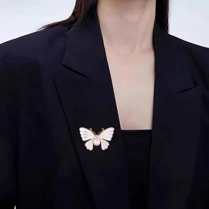 Broche papillon élégante avec perle et émail portée sur le revers d'un tailleur noir