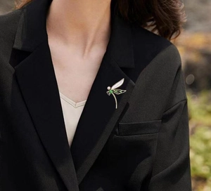 Detail der Libellen-Brosche mit grünen Steinen und Perle auf schwarzem Blazer