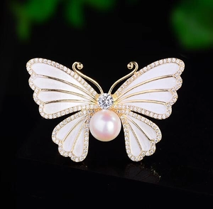 Vue macro d'une broche papillon en émail blanc ornée d'une grande perle blanche ronde