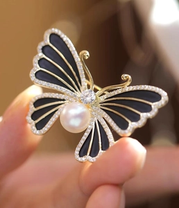 Détail d'une broche papillon avec ailes noires et finitions en perles blanches