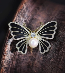 Macro de la broche papillon dorée avec émail noir, cristaux étincelants et une grande perle